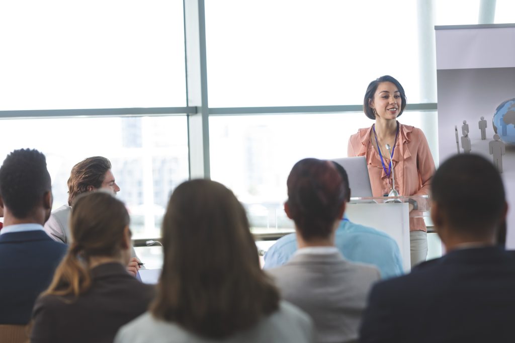 Front view of mixed-race female speaker with laptop speaks at a business seminar in office building