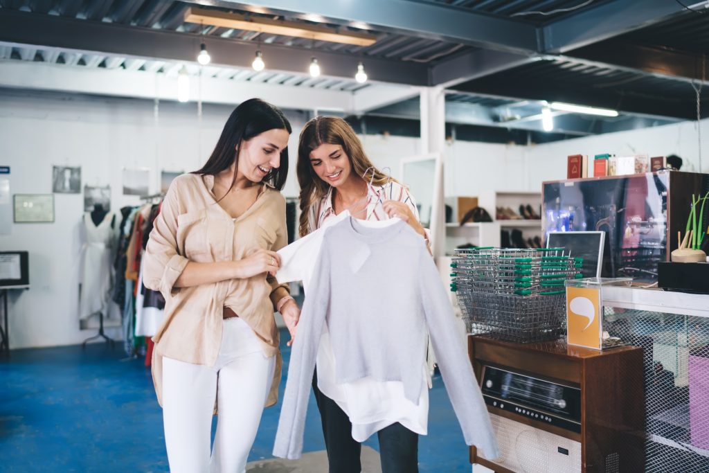 happy hipster girls with hangers discussing quality and design of purchase clothing